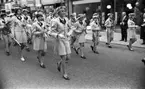 Marknadsafton 16 juni 1967

En orkester går gatan fram i centrala stan i Örebro. Den består av både kvinnor, män och ungdomar. Kvinnorna bär kavajer och kjolar och männen bär kavajer och byxor. En tamburmajor- en kvinna går framför gruppen med musikinstrument i händerna. Affärer och byggnader samt åskådare syns i bakgrunden.