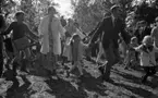 Midsommar, 26 juni 1967

Närbild på tre barn, en kvinna och en man som dansar ringdans under midsommarfirande. Kvinnan är klädd i vit kappa och mönstrad, kort klänning. Till höger om henne dansar en liten flicka i sexårsåldern med håret i pippilottor, mönstrad blus, vita strumpbyxor och mörka skor. Bredvid henne dansar en vuxen man klädd i mörk kavaj, väst, skjorta, slips och byxor. Till höger om honom dansar en liten femårig flicka med flätor, vit kappa, mörka strumpbyxor och mörka skor. Till vänster om kvinnan dansar en pojke i tioårsåldern klädd i tröja, byxor och med en stor väska över axeln.