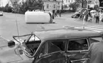 Krock 26 juni 1967

En vit buss ligger på sidan på gatan nära en refug i bakgrunden. I förgrunden syns en svart bil med intryckt sidodörr och saknad framruta. Båda fordonen har varit med om en krock. I bakgrunden till höger syns vuxna med två cyklar samt barn som betraktar olycksplatsen.