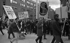 Första maj demonstration 2 maj 1967

Ett första-majtåg går genom centrala Örebro. Många personer i tåget bär på skyltar. En man har med sig ett litet barn som sitter i en barnvagn. Publik syns i bakgrunden och framför den står poliser utposterade.