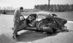 Götalundaolycka 29 maj 1967

I förgrunden syns en bil som varit med om en svår krock. Den är helt hoptryckt och står på vägen. En man klädd i grå kostym, vit skjorta och svart slips står vid sidan av bilen och blickar in i förarsätet. Framdörren på bilen står vidöppen. På andra sidan vägen i bakgrunden står en annan bil i diket och en person syns stå i närheten av denna.