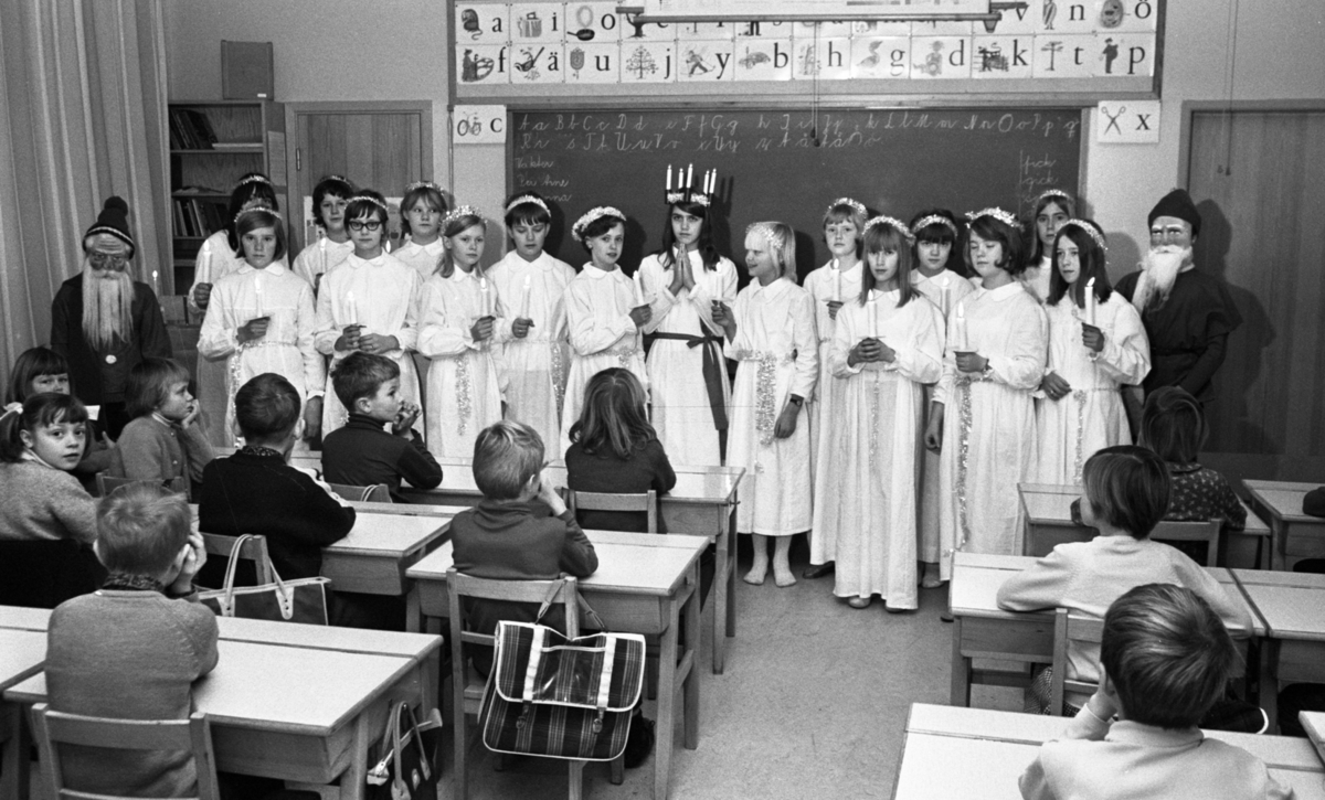 Lucia, Trafikolycka, Sörbyvägen Lillån 13 december 1966

Ett Luciatåg bestående av barn i tioåårsåldern står uppställt i ett klassrum i en skola. En Lucia befinner sig i mitten klädd i vitt linne, rött skärp om livet och ljuskrona med glitter på huvudet. Tärnorna som står runtomkring bär också vita linnen med glitter runt liven. De bär ljus i sina händer.Två tomtar står på ömse sidor om tärnorna. Framför Luciatåget sitter en publik i form av en skolklass.