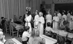 Lucia, Trafikolycka, Sörbyvägen Lillån 13 december 1966

Ett Luciatåg bestående av barn i tioåårsåldern går igenom ett klassrum i en skola. En Lucia går längst fram klädd i vitt linne, rött skärp om livet och ljuskrona med glitter på huvudet. Tärnorna som går efter Lucian bär också vita linnen med glitter runt liven. En publik i form av mellanstadieelever sitter i skolbänkarna och tittar på.