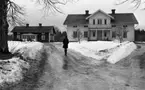 Lockhyttans herrgård, Kornbrödsbagaren, Varbergaskolan trivselskolan 17 februari 1968

Byggnader som hör till Lockhyttans herrgård varav en är en stor och vit tvåvåningsbyggnad. Den andra byggnaden är en tvåvåningsbyggnad som är röd. På den istäckta vägen går en kvinna klädd i svart kappa, svart kjol och svarta stövlar. Hon har ryggen mot kameran. Snö ligger på marken här och var.