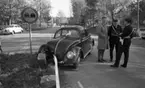 Dödsolycka i Almby 10 oktober 1967

En bil har krockat in i ett räcke och står mitt i vägen i Almby. En vägskylt syns vid gräsplätten och räcket som befinner sig mitt i gatan. En man i ljus trenchcoat, vit skjorta, svart slips, ljusa byxor och ljusa skor står och samtalar med två polismän.