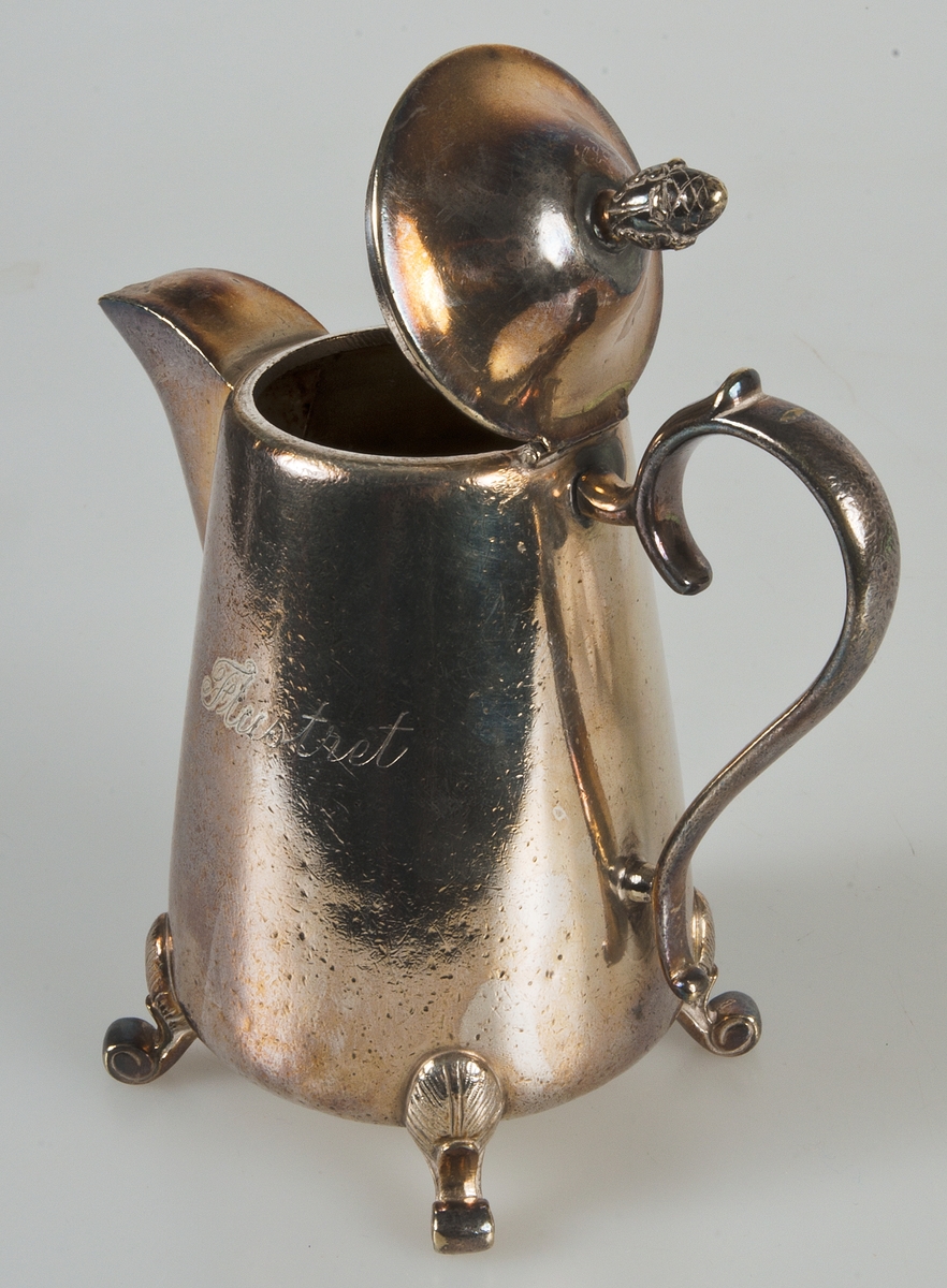 Kaffekanna, stomlödd med ilödd botten. Restaurangmodell, " grad på tassar" Rymd 50 Cl. På ena sidan graverat: Flustret. I botten stämplad: A.G. DUFVA NS R 50 cl. R: et i stämpeln ingår i Dufvas privata årsbokstavs-serie.