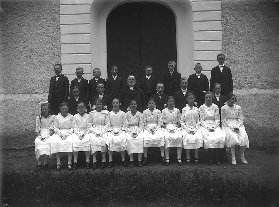 Konfirmation, konfirmander och en präst.
Kyrkobyggnad.
