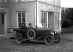 Två män i en bil.
Bostadshus. 
Bilen är en FIAT med registreringsnummer T1510. Den registrerades den 12:e maj 1922 och ägdes av chaufför Johan Anton Johansson, Örebro. Den 30:e april 1925 bytte den ägare till fabrikör J. Einar Johansson, Örebro.