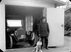 En man och en hund i garagedörren, en bil i garaget. 
Bilen är en 1912 års Overland som hade reg.nr. A1695. Den registrerades den 29:e juni 1912 och ägdes av disponent Ade Andersson, Hjortkvarn.