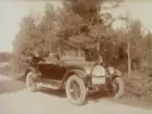 I bilen sitter Jenny Larsson med föräldrar. 
Bilen är en Oldsmobile modell 30 från 1923-24 med en 42 hästkrafters sexcylindrig motor. Den registrerades den 2:e april 1924 på fröken Jenny Larsson, Örebro, och fick registreringsnummer T99. År 1930 ägdes den fortfarande av Jenny Larsson.