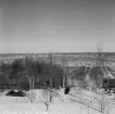 Vy. Åkermark i förgrunden, byggnader i bakgrunden.