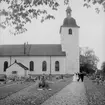 Brudpar och bröllopsgäster, kyrkobyggnad i bakgrunden.
Ragges bröllop i Stora Mellösa kyrka.