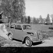 Personbil. Bostadshus till vänster på bilden.
Allmotor AB. 
Bilen är av märket Ford Anglia.