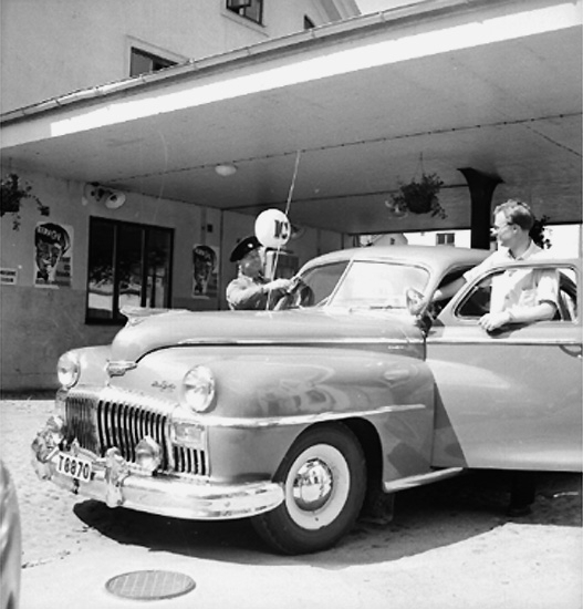 IC, besinstation, bilservice, garage.
Personbil, två män. 
Bil av märket DeSoto 1946-1948.