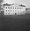 Byggnader. 
27 november 1942.
Huset var fram till 1929 Nora stads enda skolhus. 1929 byggdes färdig en ny skola vid Skolgatan. På 1950-60-talet var det rådhus.
Lilla huset bakom till vänster är Thela Bloms hattaffär. Till höger på bilden Konsum affär.