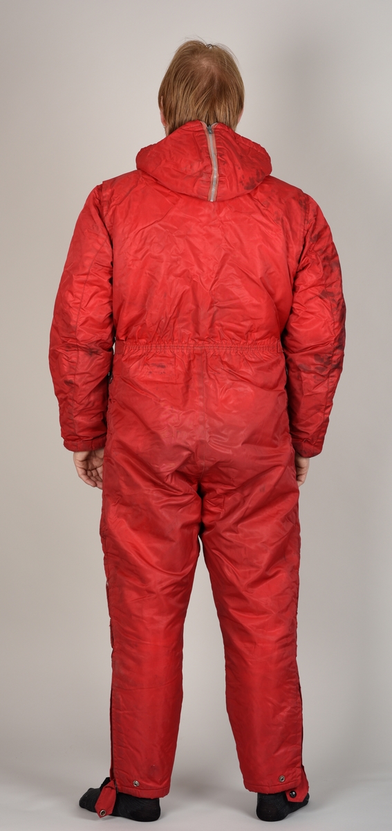 Rød dress med glidelås, hette, påsydd belte og to bukselommer.
Hetten har glidelås på oversiden.
Det er sydd på en sort stropp under hvert bein for å feste under skoene. Beltet lukkes med to halvrunde metallhemper.