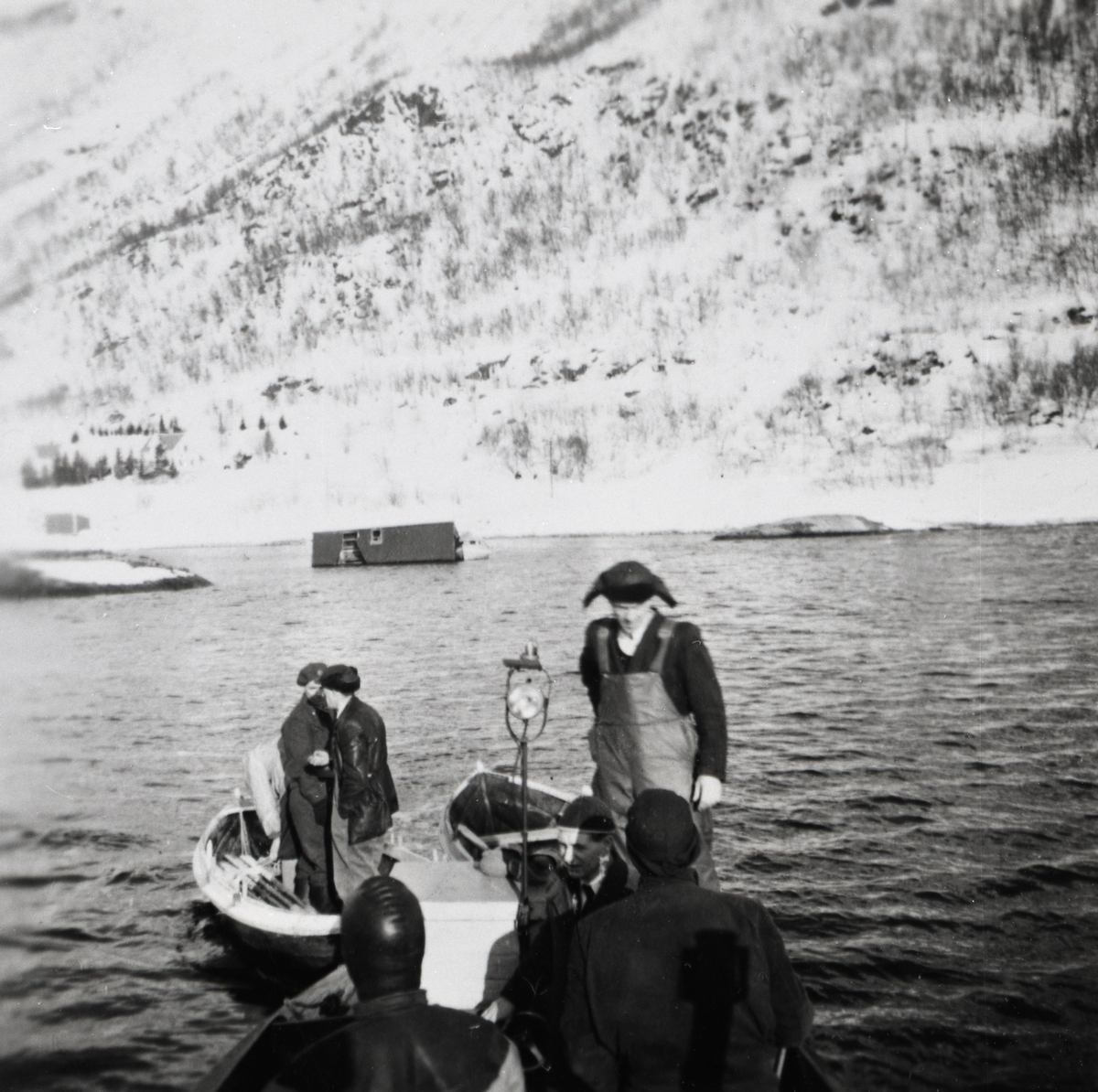 Dykkere og letemannskap i båt ved snøskredet i Sigerfjord, Sortland, vinteren 1956. Frida Breines' hus ligger ute i sjøen etter at skredet tok det. Her er dykkere og letemannskaper på tur ut til huset. Annar Pedersen står omlag midt i båten med skinnlue på hodet.