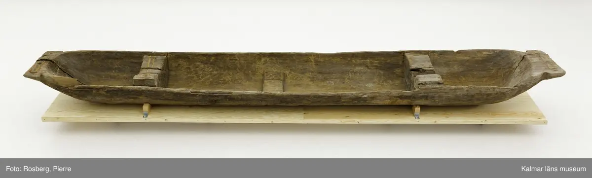 KLM 9352. Båt, stockbåt. Av stor urholkad trädstam, troligen furu. Huggen i ett stycke. Stamrunt tvärsnitt med runt, fallande överhäng. Två tofter och i mitten ett fotstöd. Går ej att uskilja för och akter. Rektangulära och rakt avskurna stävnockar, på den ena ett tamphål.