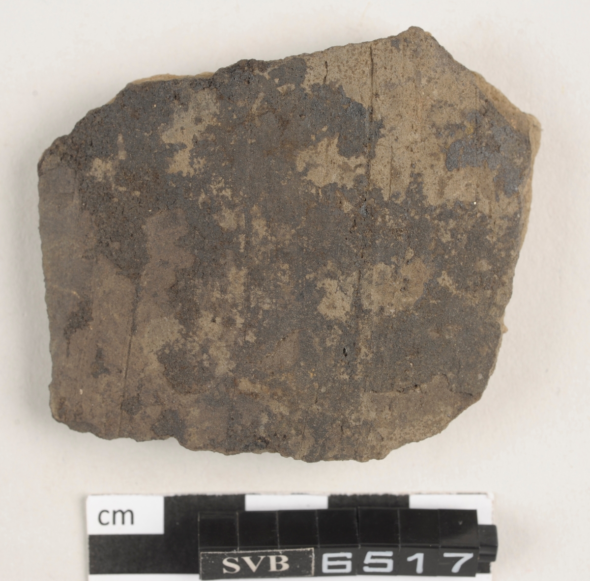 Buet keramikkfragment med bruddkanter. Fragmentet er brunt i farge.