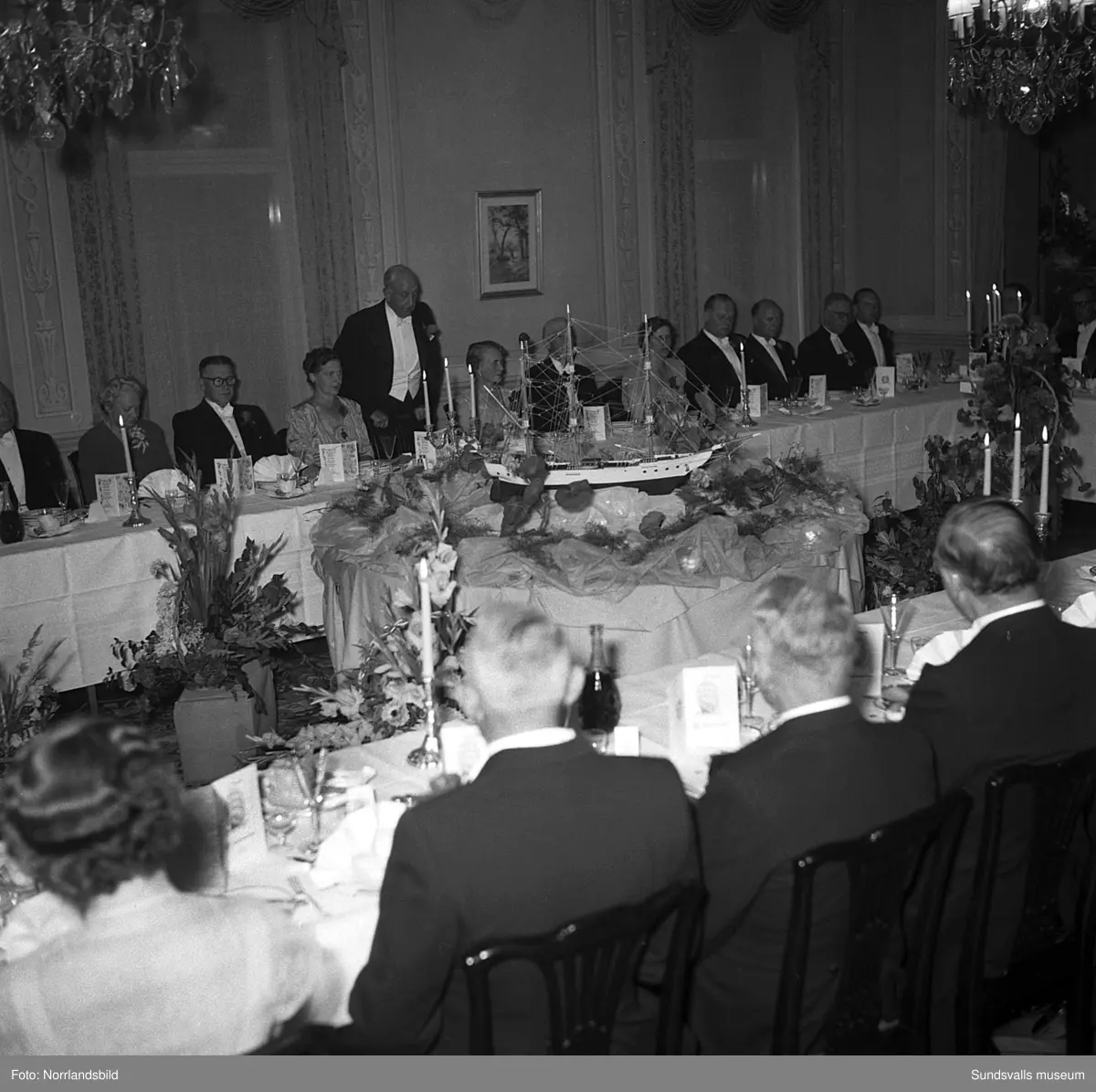 Ett urval av en stor grupp bilder från Lindgrens järnhandels 100-årsjubileumsfest på Knaust. Storstilad entré, mingel, utmärkelser, galamiddag och dans. Underhållning av bland annat en mycket ung Ingeborg Nyberg. På bilderna syns bland annat direktör Fridolf Brunnzell och lagerchefen Carl "Spiken" Lundberg, vilken samma år firade 50 år som anställd vid företaget.
