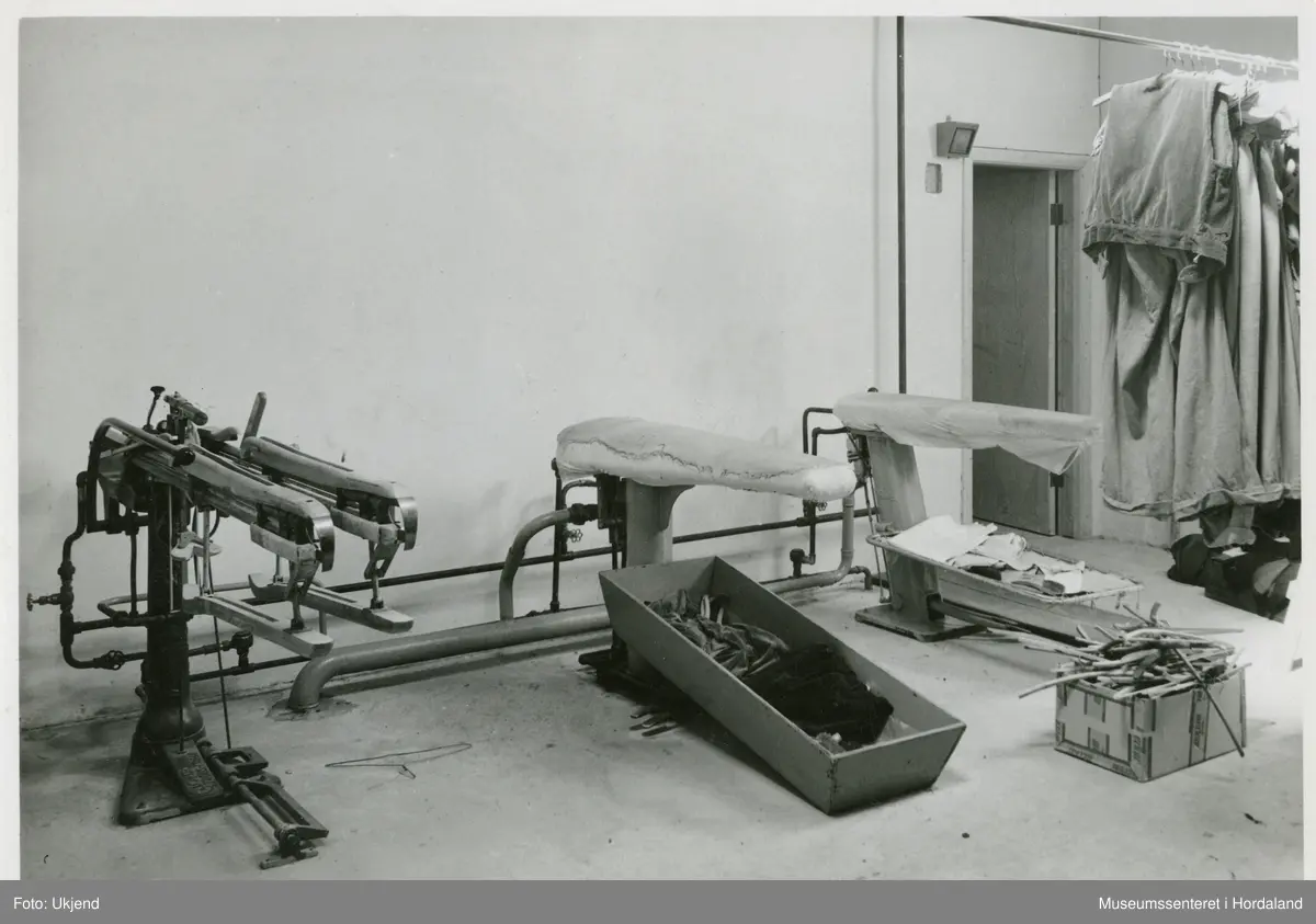 Etterbehandling av våtreinsa og farga tøy ved Wilhelm Kahrs Kemisk Renseri & Farveri, Bergen. Biletet viser "benklæ-strekker og vacuum dampbord".
