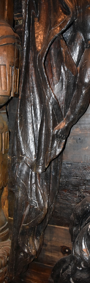 Putto samt större delen av ett draperi. Draperiet är kilformat med rak ytterkontur, och hålls undan av den svävande putton. Skulpturens baksida är slät.

Text in English: Putto and the larger part of a drapery. The drapery is wedge-shaped with straight outer contour, and is held back by the hovering putto. The reverse side is smooth.