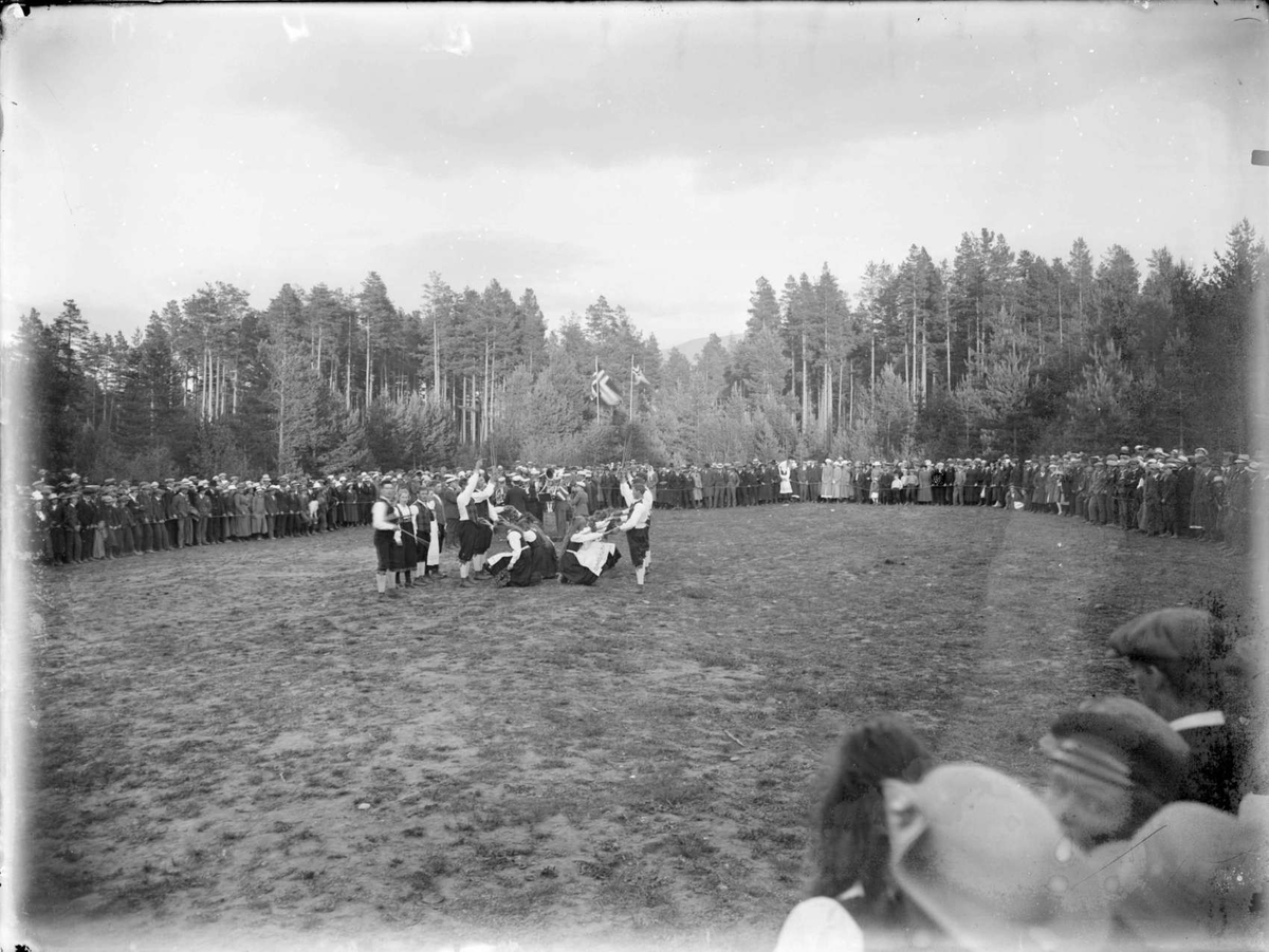 Gruppe mennesker, kvinner og menn, festkledde, leikarring,åpen plass, skog, (sang/musikkstevne?) (Kåja?)