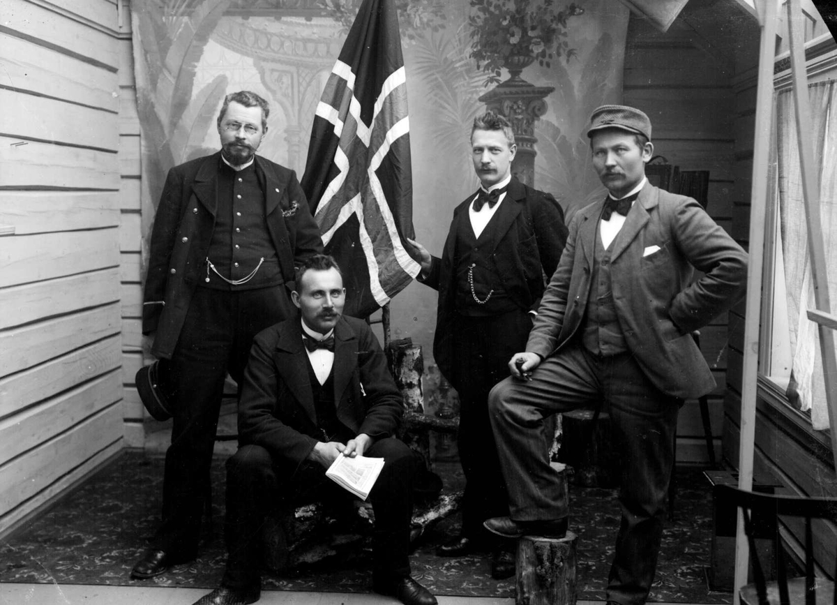 Atelierbilde av fire menn, en av de i uniform, norsk flagg
