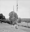 Festligheter vid Siggebohyttan den 1 augusti 1937. På grässlänten intill Siggebohyttans bergsmansgård står en talare i en talarstol och håller ett anförande. På bägge sidor om talaren står varsin flaggstång med en svensk flagga. Likaså talarstolen är iklädd en svensk flagga. Till vänster på grässlänten syns några åskådare.