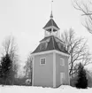 Bystad (Bysta) den 23 mars 1937. Den fristående klockstapeln, som hör till kyrkan, är gjord av trä och målad i gul färg (framgår ej av bilden). På det nedre takets alla fyra sidor finns varsin klocka med urtavla. Över det nedre taket finns själva kyrkklockan i ett utrymme med fria öppningar ut, och längst upp ett övre tak med en liten lökkupol och en vindflöjel. På vindflöjeln står det 