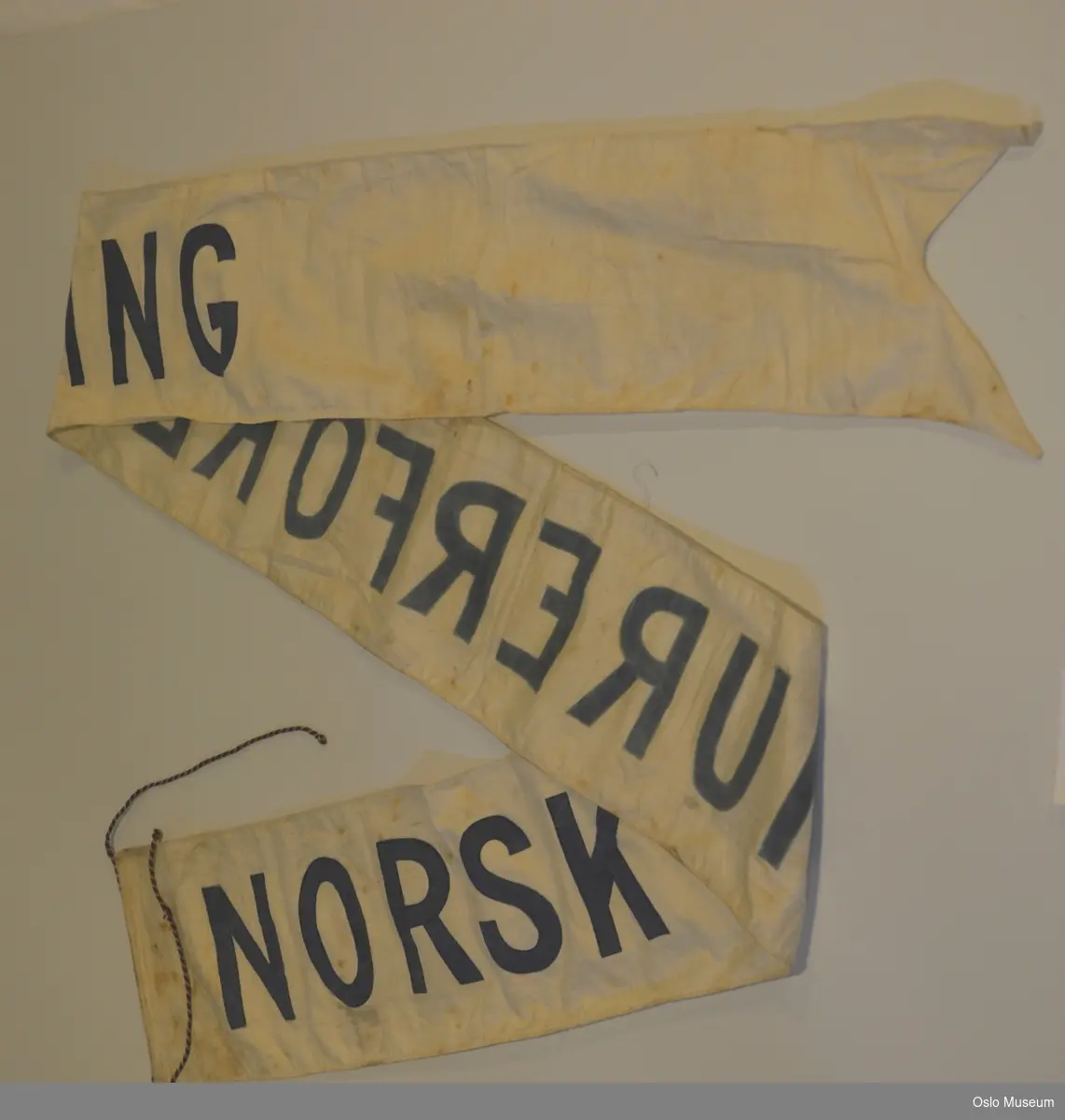 Banner for Norsk Murerforening i hvitt silkestoff med snorer i ene enden og to tunger i den andre enden.