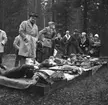 Samrealelever vid skjutbanan.
Stående i rock och hatt magister L. Ranch.
Miltärklädd, Gunnar Granberg.
Skolfröken som antecknar, Kerstin Rickardsson.