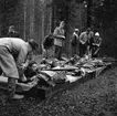 Samrealelever vid skjutbanan.
Stående i rock och hatt magister L. Ranch.
Miltärklädd, Gunnar Granberg.
Skolfröken som antecknar, Kerstin Rickardsson.