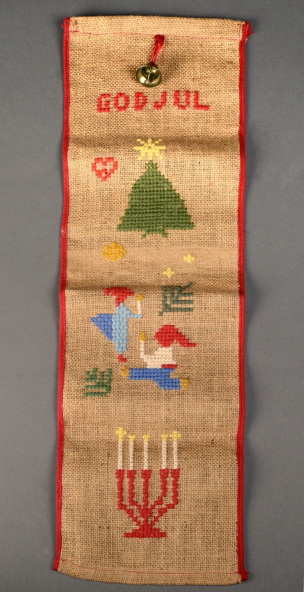 Klokkestreng i brun strie brodert med grov ulltråd. Øverst er det sydd på en messingbjelle som henger i en rød silketråd. Under er det brodert GOD JUL og deretter et juletre, to nissefigurer og til slutt en lysestake med fem lys i. Røde kantbånd er sydd på (maskinsydd) på langsidene. Oppe og nede er det maskinsydd kant.