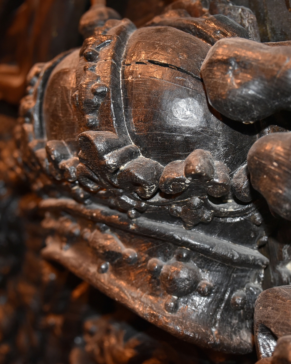 Skulpterad, kunglig krona. Undersidan är perspektiviskt framställd genom att kronans baksida gjorts högre än framsidan. Kronringen är upptill prydd med omväxlande större och mindre liljeliknande ornament. På själva ringen och på byglarna sitter fasettslipade "ädelstenar". Kronans baksida är slät.
Kronan är välbevarad.

Text in English: Royal crown. The underside is carved in perspective, achieved by carving the back of the crown higher than the front. The circlet is decorated at the top with lily-like ornaments of varying size. On the circlet itself and on the verticals are faceted "precious stones". The reverse side of the crown is smooth.
The sculpture is well preserved.