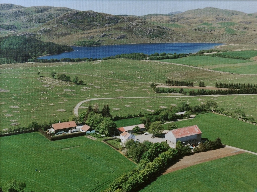 Flyfoto av Heiane bruk 8 av Sæland. Hovedbuset midt i, løa til høgre og kårbygget til venstre. Bak det ser ein det freda fornminnefeltet "Lyngaland" og bak der att Melsvatnet.