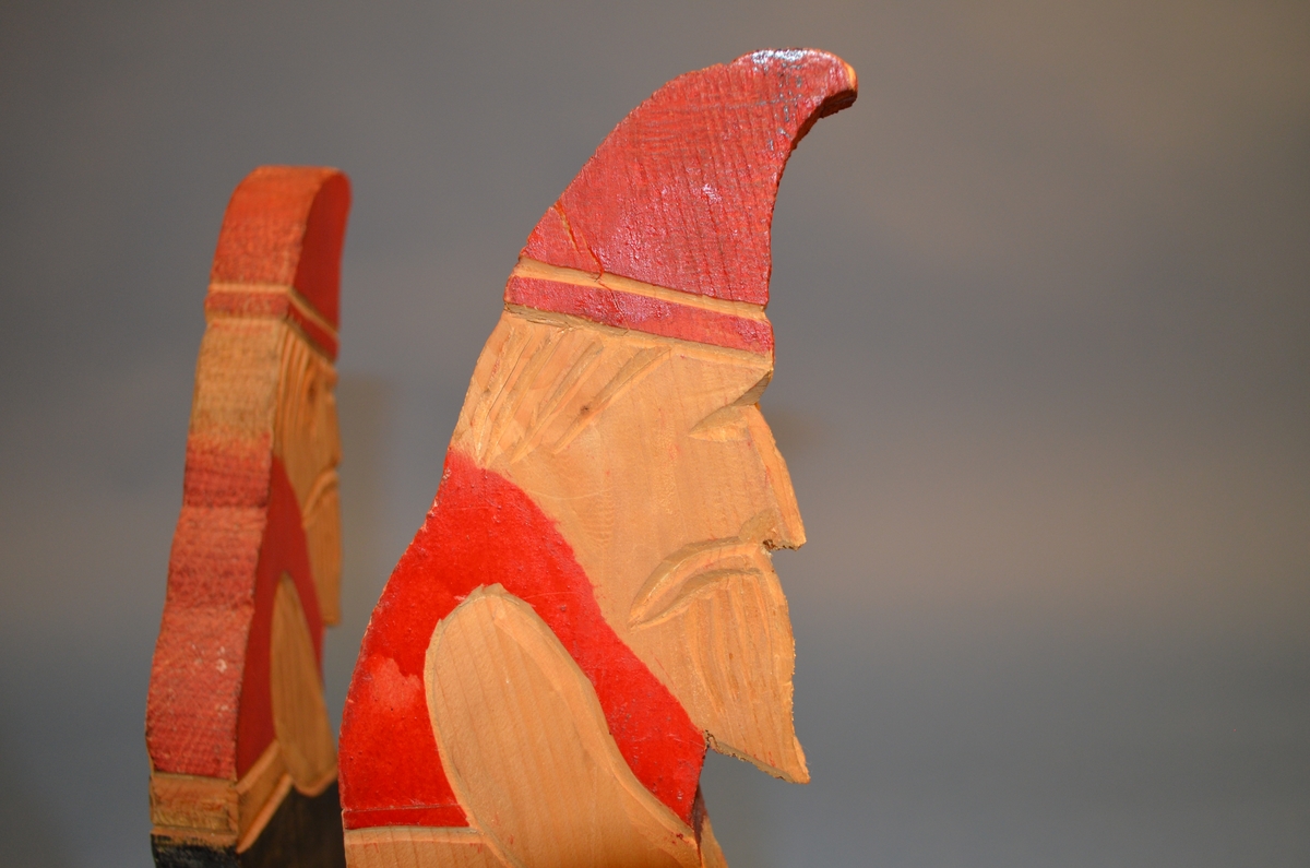 Hjemmelaget juletrefot av tre. Foten er satt sammen av tre støtter av hele trestykker formet som sittende nisser. I midten er et sirkelformet trestykke med hull for selve juletreet. Støtter og midtstykket er satt sammen med spiker. Juletrefoten er håndmalt. Nissene er malt i rødt og svart. Midtstykket grønt, med rosa underside.