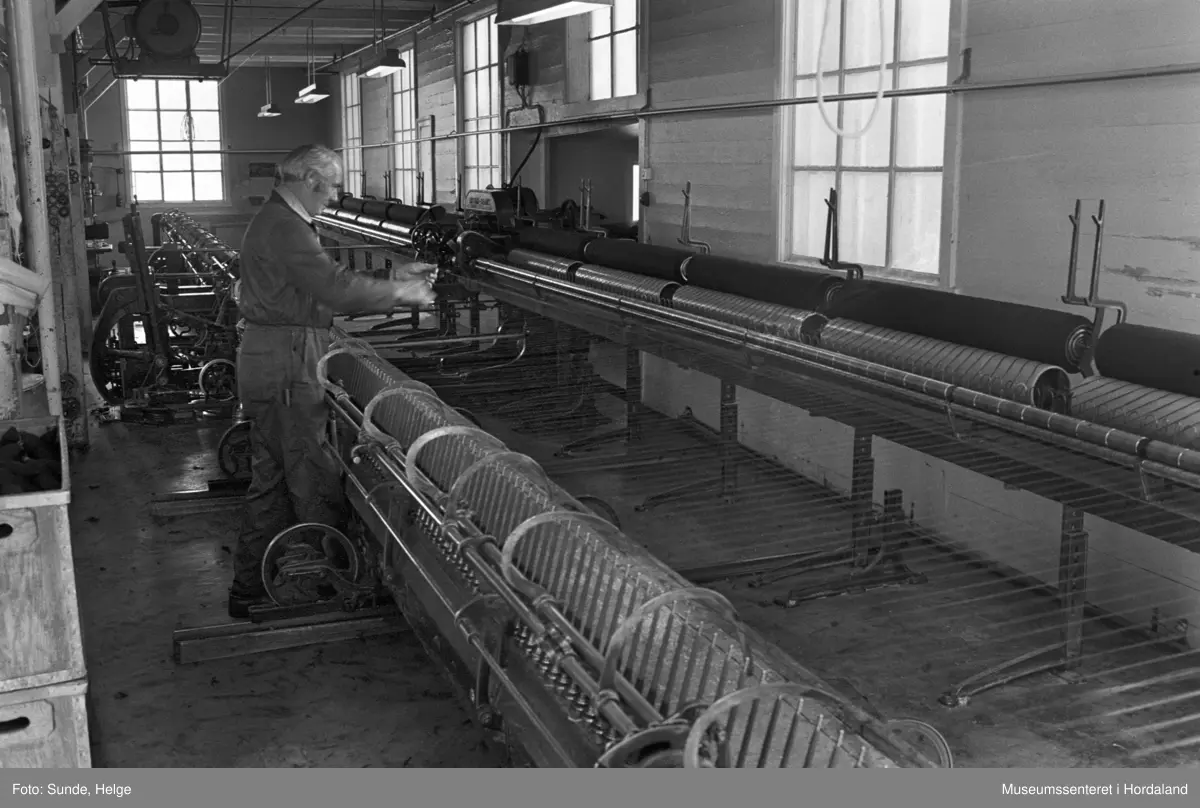 Arbeidsliv ved Salhus Tricotagefabrik i Salhus, Bergen i 1976. Arbeidar ved selfaktor (spinnemaskin) i 1900-bygget ved Salhus Tricotagefabrik.