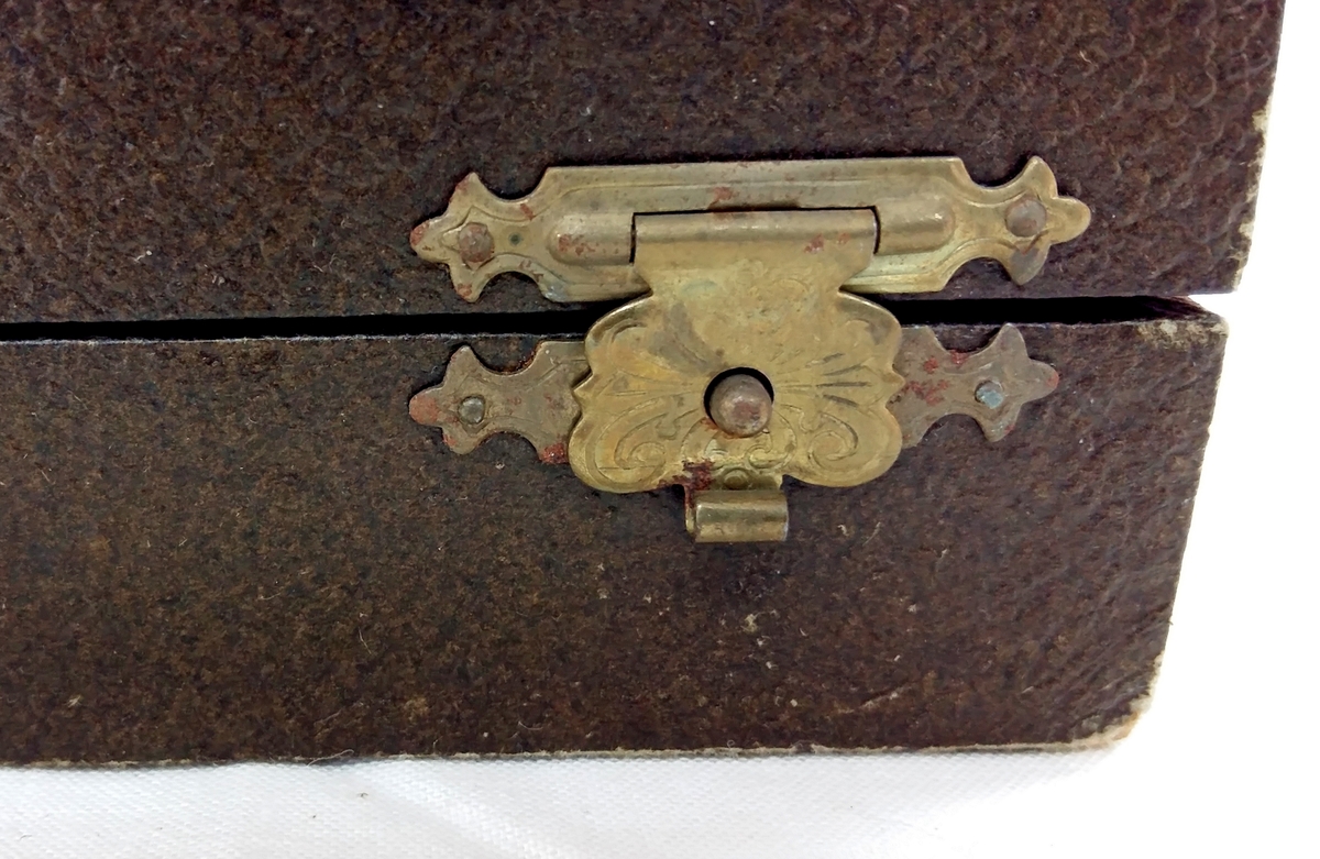Etui for bestikk. Imitert, svart skinn. Svart øskje med lok hengsla på. Metallukking i gult metall. Fôr i silke i lok. Fôr i flanell i botn. Plass til 12 delar.