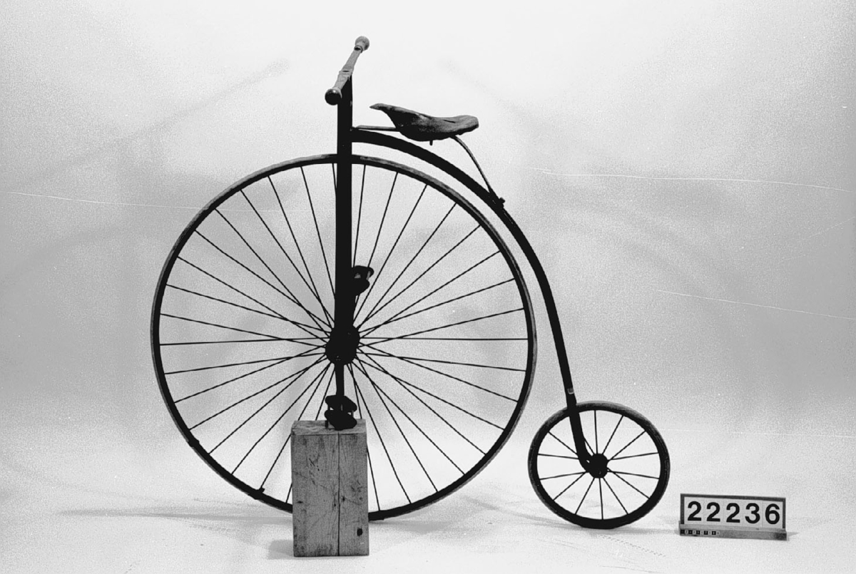 Höghjulig, mindre modell, med framgaffel av plattjärn och originalgummi på bakhjulet.
Tillbehör: Ringklocka och verktygsväska.