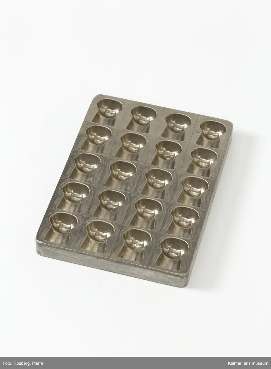 KLM45785:1. Form. Av tenn. Gjutform för chokladpraliner. Formen för pralinerna förefaller vara en champagnekork. 20 praliner finns det plats för att gjuta i formen. På ena långsidan text, Anton Reiche Dresden Nacn No 16640.