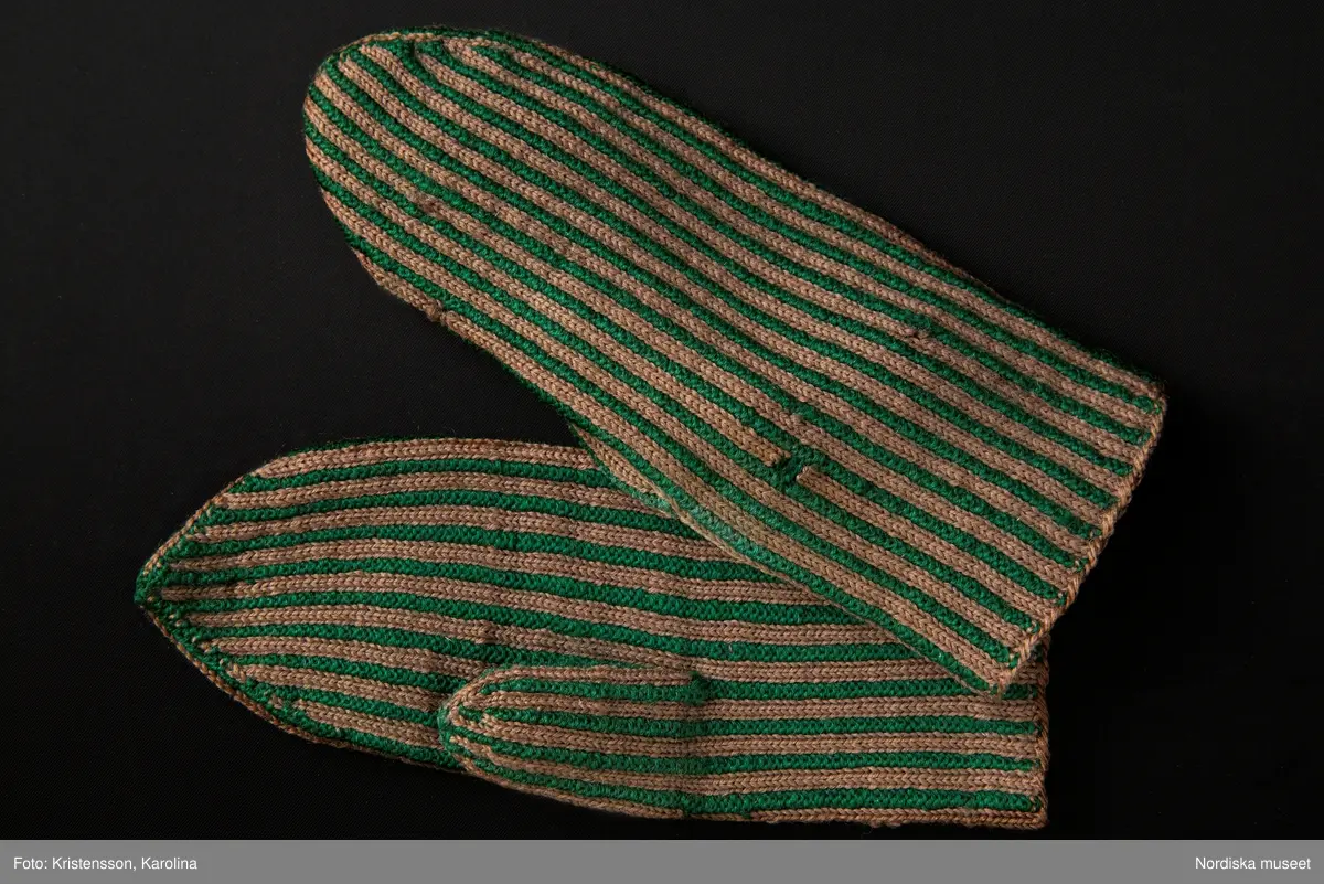 Ett par kvinnovantar stickade av ullgarn, smalrandiga i grönt och ljusbrunt. De ljusbruna ränderna består av 2 maskor slätstickning och de gröna av 2 aviga  maskor,  där de 2 färgerna  hela tiden följer med  och flotterar på avigsidan. Det ger en stum yta utan elasticitet. 
Anm Den högra vanten mer sliten med flera stoppningar med det gröna garnet.
Har tillhört Augusta Davidsson, "Snögges Augusta" f. 1868 i Habo död 1950 på ålderdomshemmet. Hon hade bott hela sitt liv i föräldrahemmet ett soldattorp under Vagnhult i Habo. hennes far var soldat liksom brodern Efraim. Först vårdade hon modern i hemmet, senare hushållade hon åt den ogifte brodern Efraim. Sen gick hon på "hjälpe" hos bönderna i bygden. Foto av stugan skall finnas i museet. Kläderna som museet mottagit är de som hon hade med sig till ålderdomshemmet.
/Berit Eldvik 2013-03-11