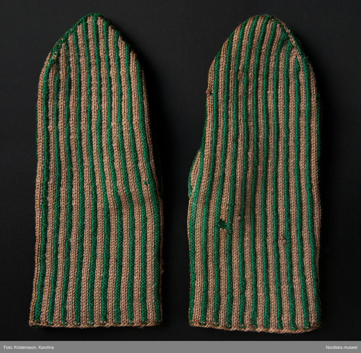 Ett par kvinnovantar stickade av ullgarn, smalrandiga i grönt och ljusbrunt. De ljusbruna ränderna består av 2 maskor slätstickning och de gröna av 2 aviga  maskor,  där de 2 färgerna  hela tiden följer med  och flotterar på avigsidan. Det ger en stum yta utan elasticitet. 
Anm Den högra vanten mer sliten med flera stoppningar med det gröna garnet.
Har tillhört Augusta Davidsson, "Snögges Augusta" f. 1868 i Habo död 1950 på ålderdomshemmet. Hon hade bott hela sitt liv i föräldrahemmet ett soldattorp under Vagnhult i Habo. hennes far var soldat liksom brodern Efraim. Först vårdade hon modern i hemmet, senare hushållade hon åt den ogifte brodern Efraim. Sen gick hon på "hjälpe" hos bönderna i bygden. Foto av stugan skall finnas i museet. Kläderna som museet mottagit är de som hon hade med sig till ålderdomshemmet.
/Berit Eldvik 2013-03-11