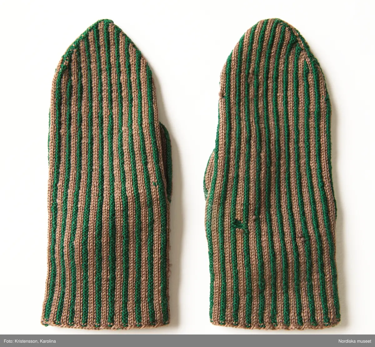 Ett par kvinnovantar stickade av ullgarn, smalrandiga i grönt och ljusbrunt. De ljusbruna ränderna består av 2 maskor slätstickning och de gröna av 2 aviga  maskor,  där de 2 färgerna  hela tiden följer med  och flotterar på avigsidan. Det ger en stum yta utan elasticitet. 
Anm Den högra vanten mer sliten med flera stoppningar med det gröna garnet.
Har tillhört Augusta Davidsson, "Snögges Augusta" f. 1868 i Habo död 1950 på ålderdomshemmet. Hon hade bott hela sitt liv i föräldrahemmet ett soldattorp under Vagnhult i Habo. hennes far var soldat liksom brodern Efraim. Först vårdade hon modern i hemmet, senare hushållade hon åt den ogifte brodern Efraim. Sen gick hon på "hjälpe" hos bönderna i bygden. Foto av stugan skall finnas i museet. Kläderna som museet mottagit är de som hon hade med sig till ålderdomshemmet.
/Berit Eldvik 2013-03-11