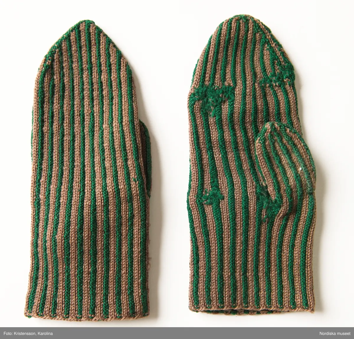 Ett par kvinnovantar stickade av ullgarn, smalrandiga i grönt och ljusbrunt. De ljusbruna ränderna består av 2 maskor slätstickning och de gröna av 2 aviga  maskor,  där de 2 färgerna  hela tiden följer med  och flotterar på avigsidan. Det ger en stum yta utan elasticitet. 
Anm Den högra vanten mer sliten med flera stoppningar med det gröna garnet.
Har tillhört Augusta Davidsson, "Snögges Augusta" f. 1868 i Habo död 1950 på ålderdomshemmet. Hon hade bott hela sitt liv i föräldrahemmet ett soldattorp under Vagnhult i Habo. hennes far var soldat liksom brodern Efraim. Först vårdade hon modern i hemmet, senare hushållade hon åt den ogifte brodern Efraim. Sen gick hon på "hjälpe" hos bönderna i bygden. Foto av stugan skall finnas i museet. Kläderna som museet mottagit är de som hon hade med sig till ålderdomshemmet.
/Berit Eldvik 2013-03-11