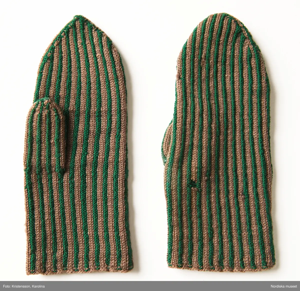 Ett par kvinnovantar stickade av ullgarn, smalrandiga i grönt och ljusbrunt. De ljusbruna ränderna består av 2 maskor slätstickning och de gröna av 2 aviga  maskor,  där de 2 färgerna  hela tiden följer med  och flotterar på avigsidan. Det ger en stum yta utan elasticitet. 
Anm Den högra vanten mer sliten med flera stoppningar med det gröna garnet.
Har tillhört Augusta Davidsson, "Snögges Augusta" f. 1868 i Habo död 1950 på ålderdomshemmet. Hon hade bott hela sitt liv i föräldrahemmet ett soldattorp under Vagnhult i Habo. hennes far var soldat liksom brodern Efraim. Först vårdade hon modern i hemmet, senare hushållade hon åt den ogifte brodern Efraim. Sen gick hon på "hjälpe" hos bönderna i bygden. Foto av stugan skall finnas i museet. Kläderna som museet mottagit är de som hon hade med sig till ålderdomshemmet.
/Berit Eldvik 2013-03-11