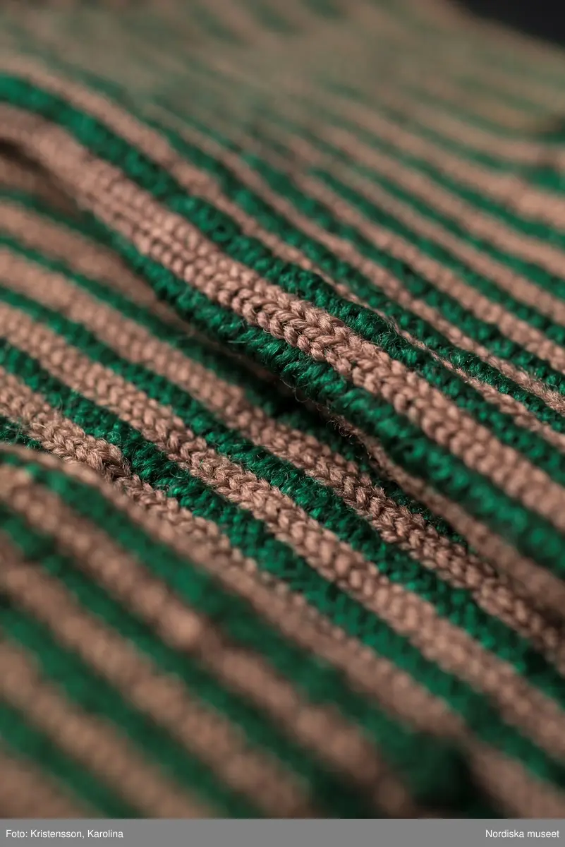 Ett par kvinnovantar stickade av ullgarn, smalrandiga i grönt och ljusbrunt. De ljusbruna ränderna består av 2 maskor slätstickning och de gröna av 2 aviga  maskor,  där de 2 färgerna  hela tiden följer med  och flotterar på avigsidan. Det ger en stum yta utan elasticitet. 
Anm Den högra vanten mer sliten med flera stoppningar med det gröna garnet.
Har tillhört Augusta Davidsson, "Snögges Augusta" f. 1868 i Habo död 1950 på ålderdomshemmet. Hon hade bott hela sitt liv i föräldrahemmet ett soldattorp under Vagnhult i Habo. hennes far var soldat liksom brodern Efraim. Först vårdade hon modern i hemmet, senare hushållade hon åt den ogifte brodern Efraim. Sen gick hon på "hjälpe" hos bönderna i bygden. Foto av stugan skall finnas i museet. Kläderna som museet mottagit är de som hon hade med sig till ålderdomshemmet.
/Berit Eldvik 2013-03-11