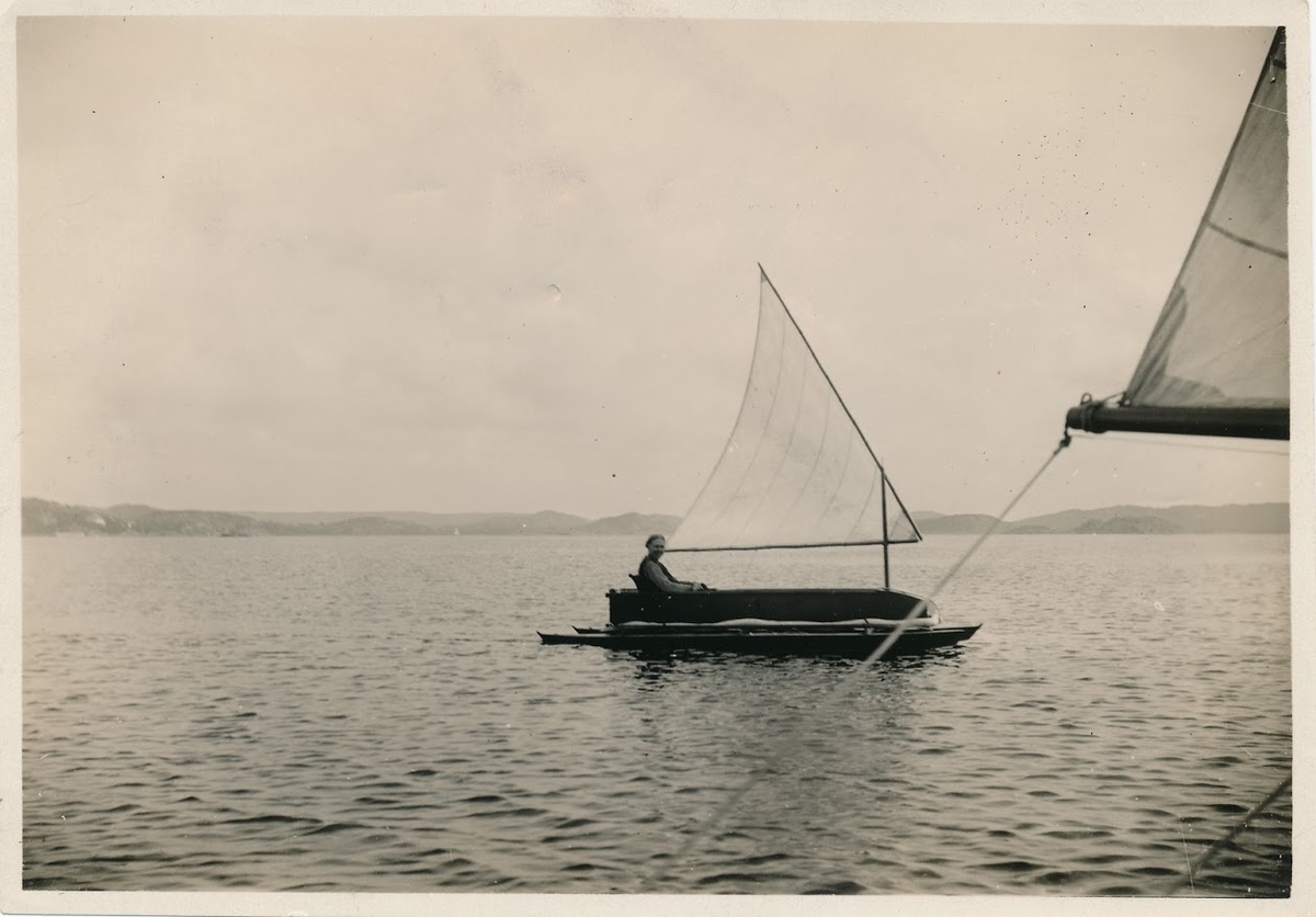 Tidig katamaran, omkr 1910, byggd i Frankrike. Pontonerna möjligen tillverkade av mahognyplywood. Sittbrunnen (lådan) har botten i trä och sidor i kraftig duk. Inspektionsluckorna på pontonernas ovansida saknar lock. Lucka i durken i främre delen av sittbrunnen. Runt sittbrunnen löper någon slags (gissningsvis) flytanordning. 
Lösa tillbehör:
Sits med ryggstöd 
Fyra roder 
Fem rorkultar 
Tre master i olika längd
Två, längre, delbara paddlar
Två kortare paddlar med en slags uppblåsbar flytanordning på mitten.
Två segel i tunn bomull, litsade till rundhult i bambu.