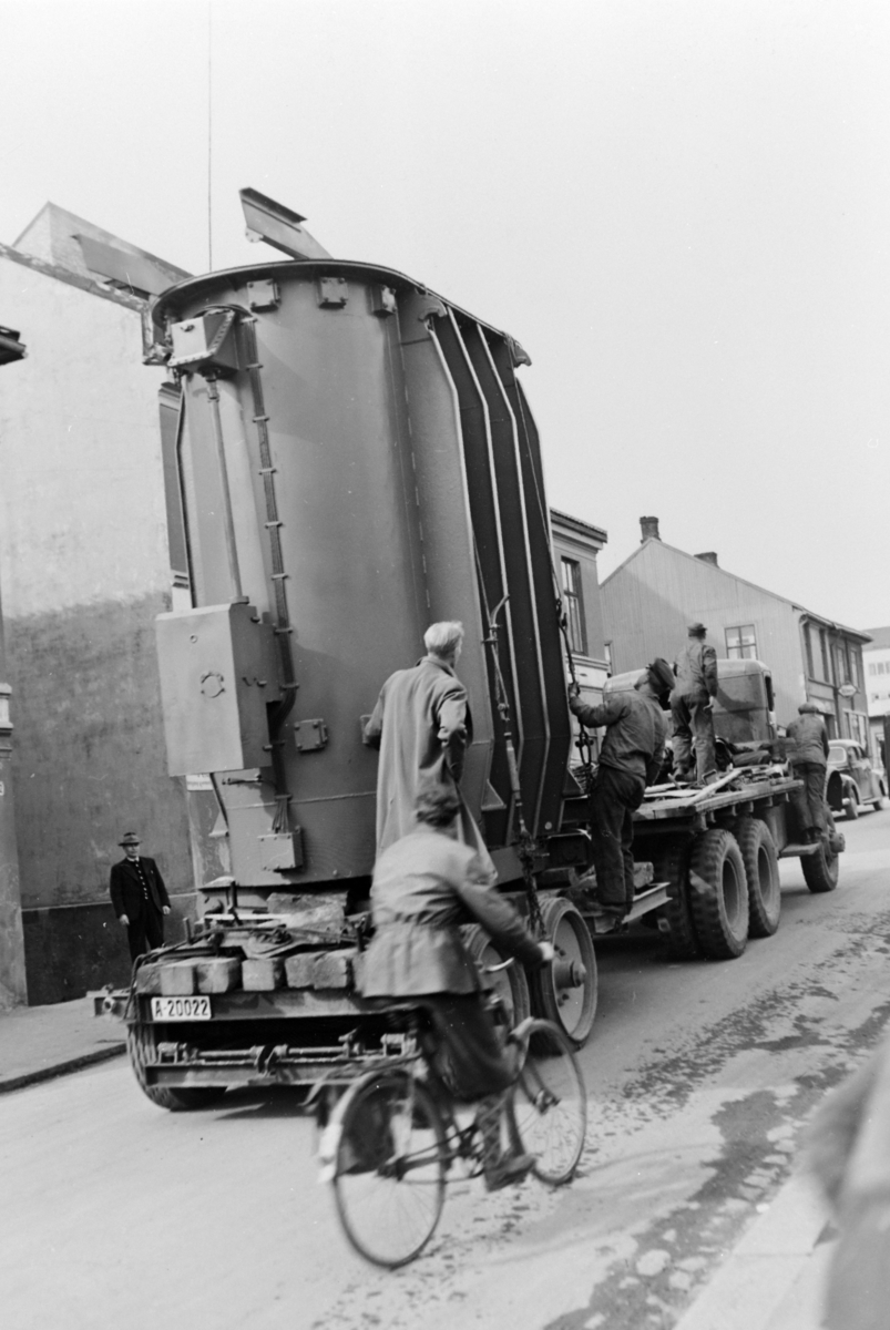Grønnegata i Hamar. Frakt av 10 MVA transformator til Børstad våren 1949. Transport utført av Fridtjof Kristiansen spedisjon, Oslo. Trekkvogn av merke Mack, type NM, 1943 modell.  Bilens reg-nr er A-44735.Lastebil med folk fra kraftselskapet overvåker transporten. Trekkvogn, tilhenger, A-20022, tungtransport. Hamar Vang og Furnes kommunale kraftselskap.