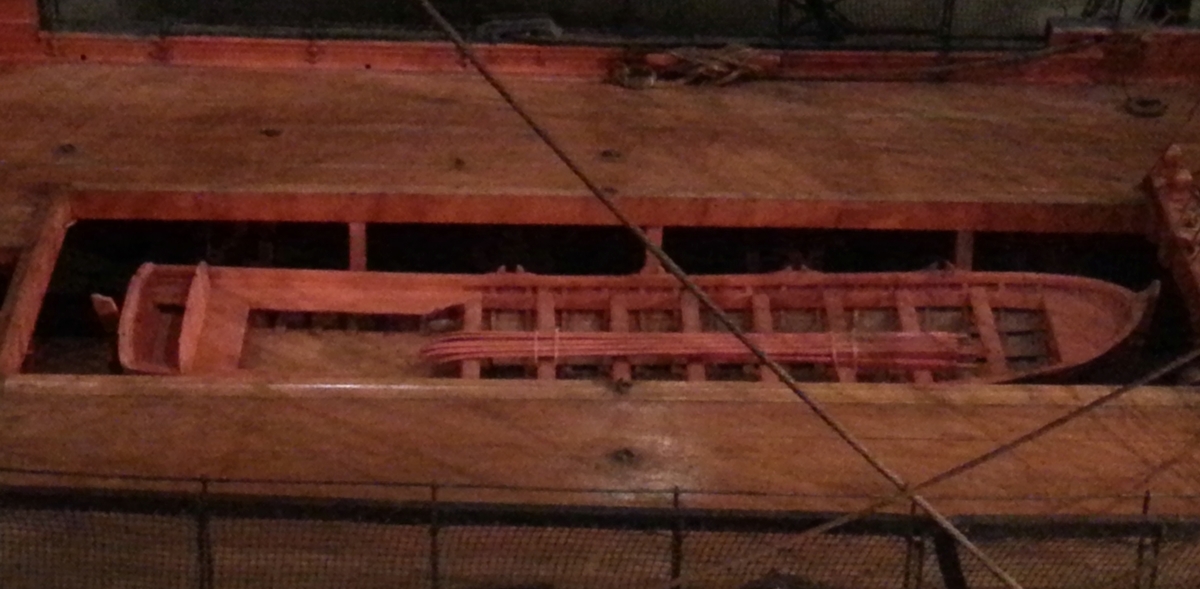 Båtmodell, gigg, bordlagd på spant, kravell, med fullständig inredning. Roder med rorkult . 9 st årtullar. 9 st åror. Fernissad med röd reling, svart sugband.   Åror, bänkar och sittrum rödmålade. Innerbotten och trall fernissade. Stativ brunmålat.